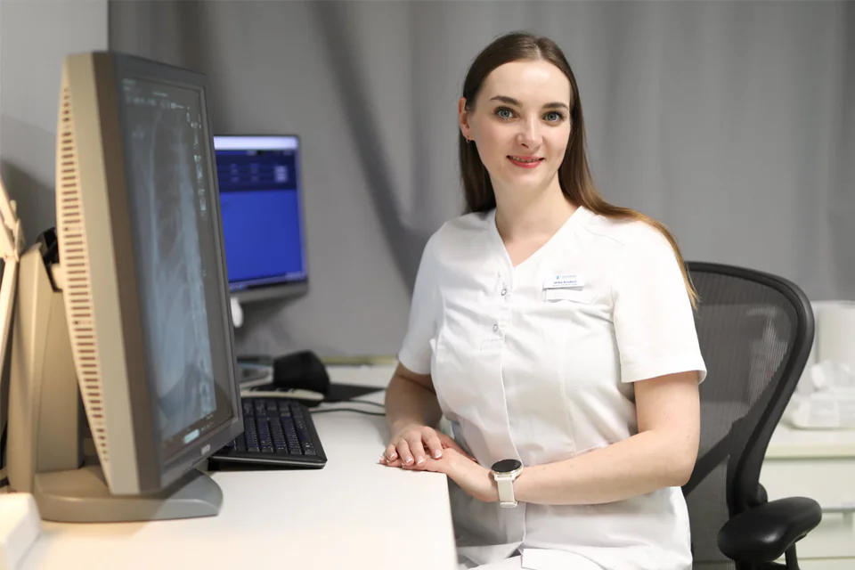 A medical professional in a clinical setting with an x-ray image on the screen.